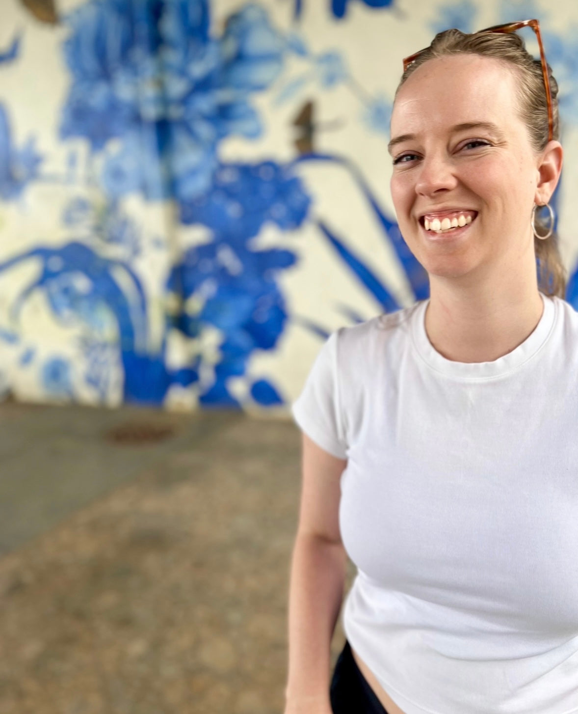 The founder of Witness the Earth artwork store, Julia, smiles for a photo in front of a wall with a floral mural